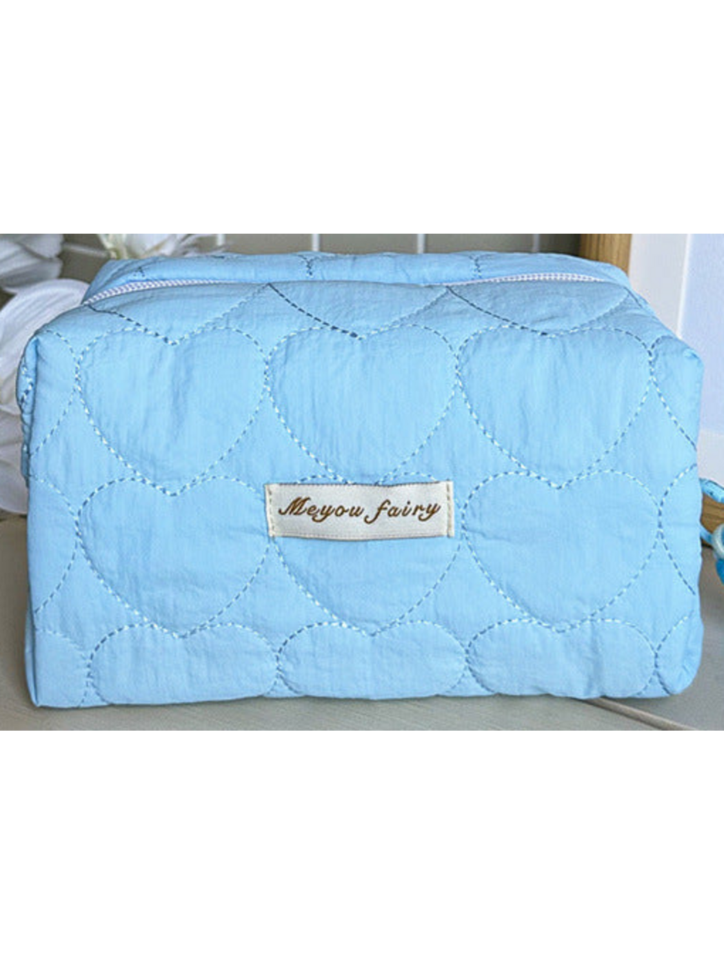Blue heart-quilted pouch body with white zipper and sewn label; limited detail view