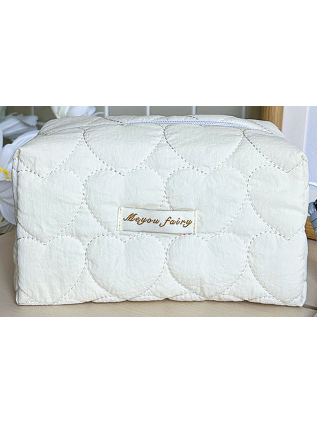 Ivory heart-quilted pouch body with white zipper and sewn label; limited detail view