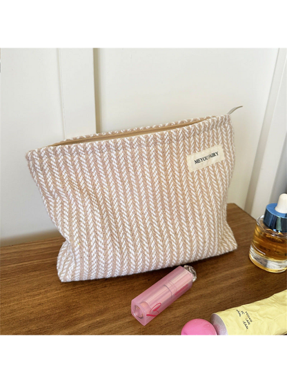 Beige makeup pouch with contrasting white textured stripes, upright view