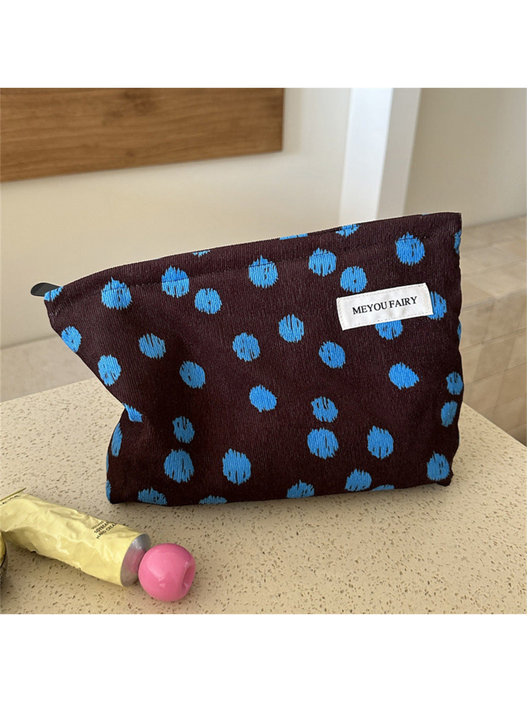 Brown cosmetic bag with irregular blue dots, standing on a countertop