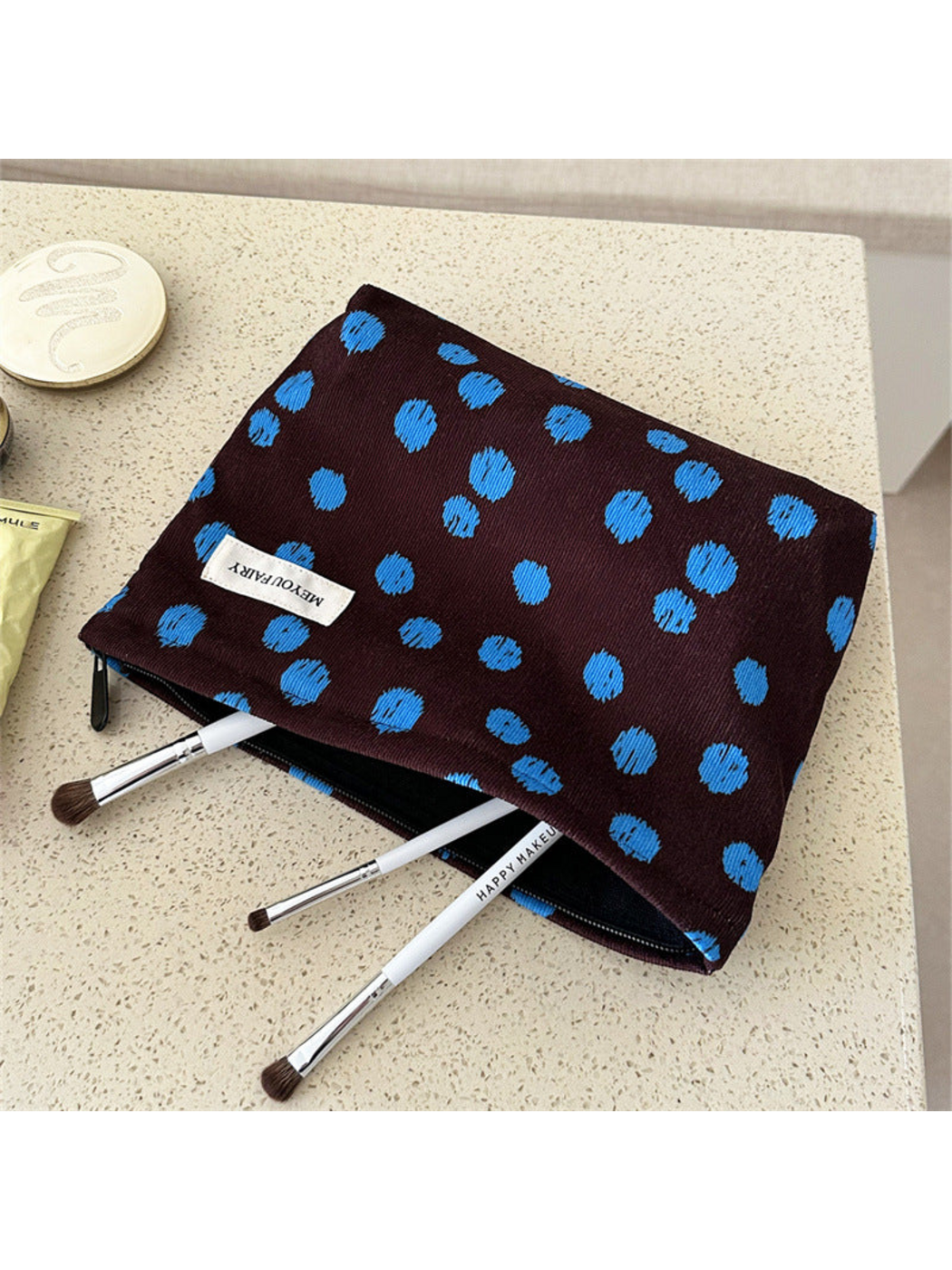 Brown cosmetic bag with blue dots, lying open with makeup brushes at the opening