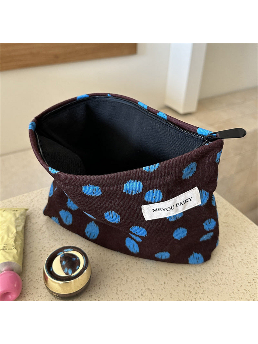 Brown cosmetic bag with blue dots, open to show the black interior