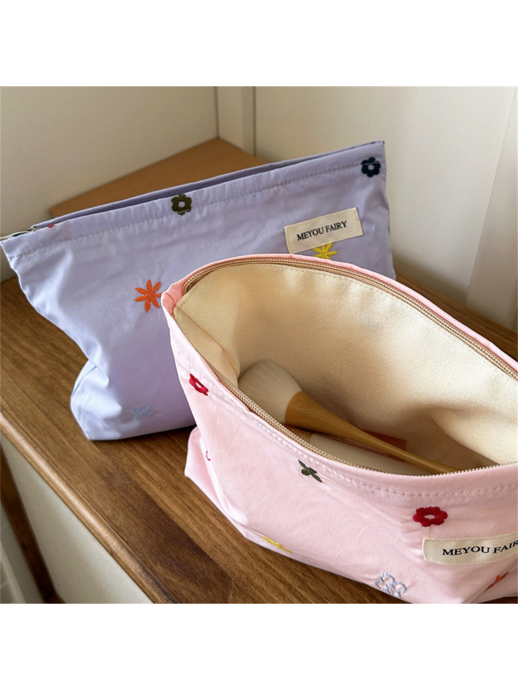 Open Pink floral makeup bag showing cream-colored lining and a brush prop, with Purple bag behind