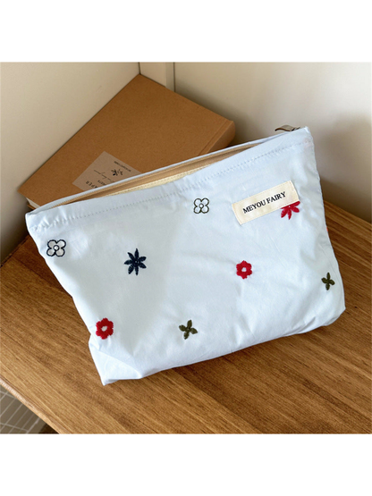 Blue makeup bag with scattered multicolored embroidered flowers, front view