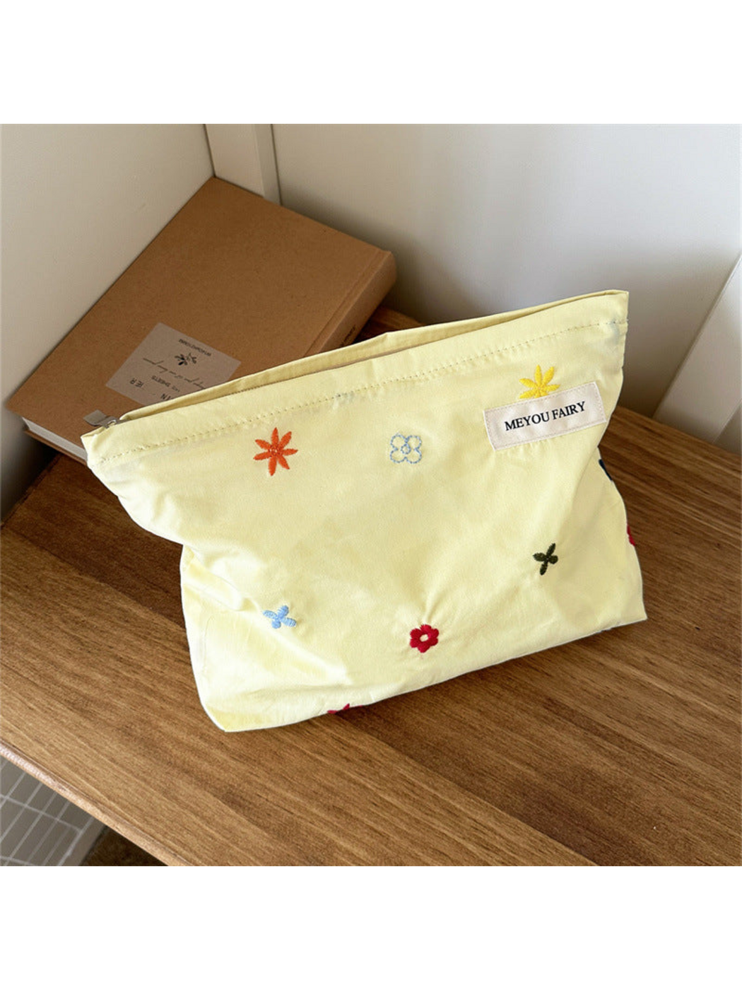 Yellow makeup bag with scattered multicolored embroidered flowers, front view