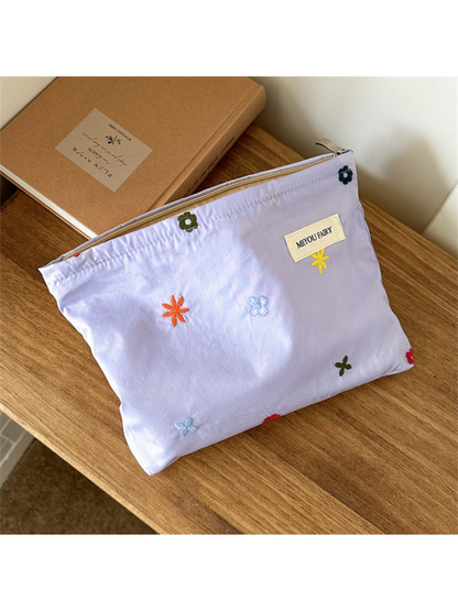 Purple makeup bag with scattered multicolored embroidered flowers, angled front view