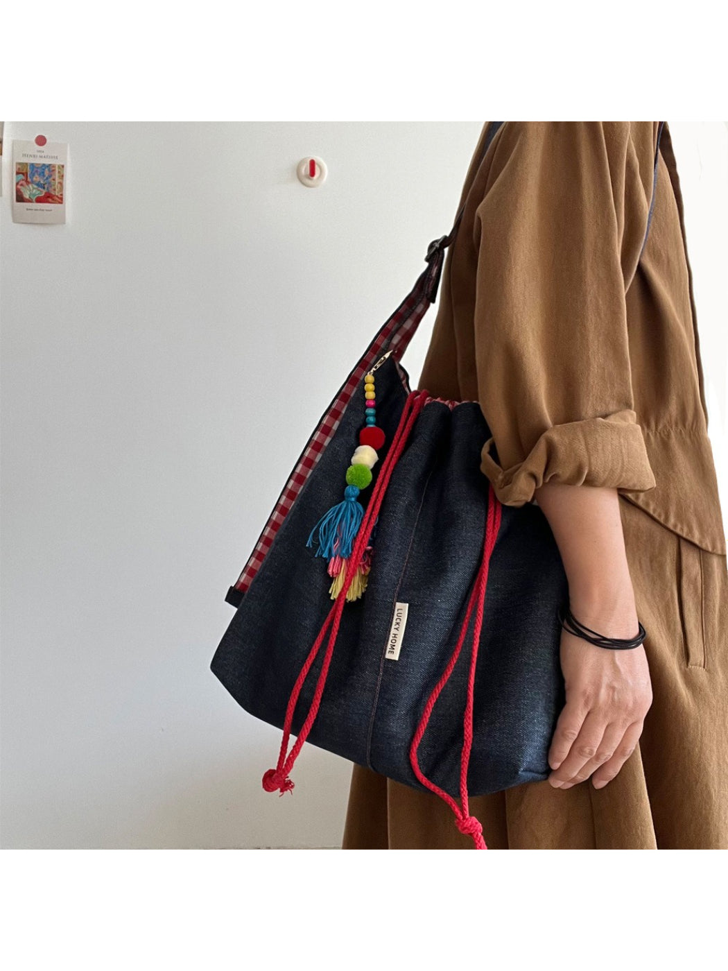 Side view of Cosbai bucket bag showing gingham trim and tassel details