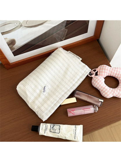 Striped cosmetic bag with plush charm placed on wooden surface