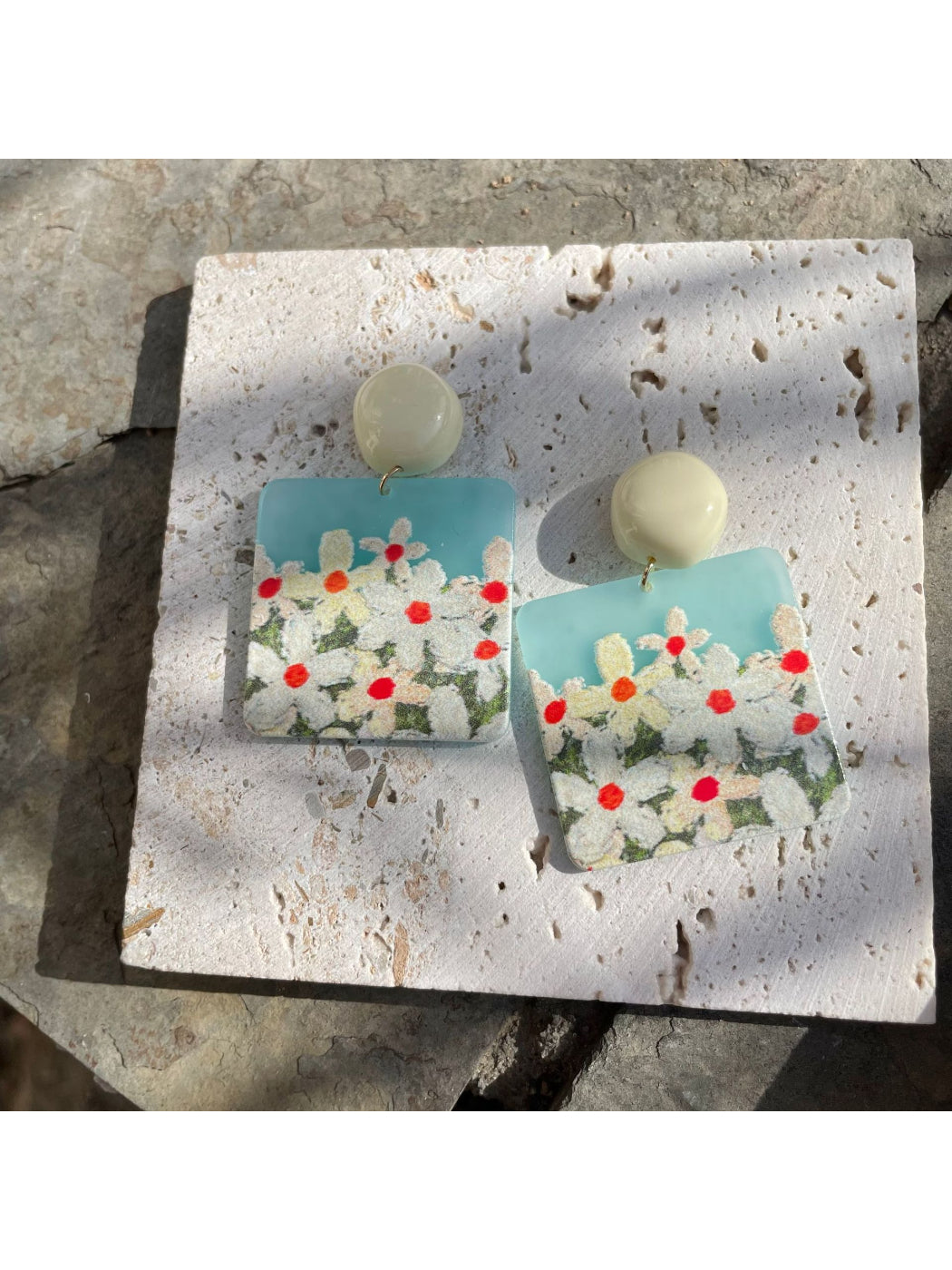 Pair of Earwish Daisy Field drop earrings placed on a wooden surface