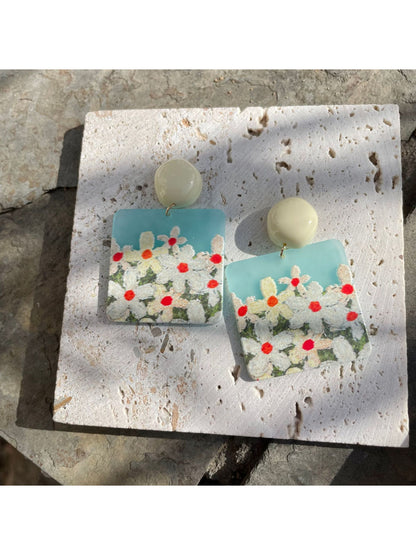 Pair of Earwish Daisy Field drop earrings placed on a wooden surface