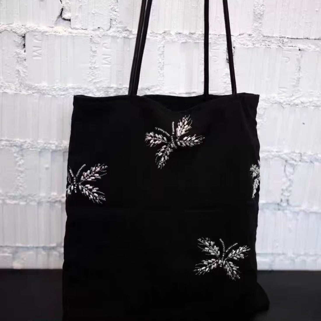 Side view of black tote bag with beaded detail and handles