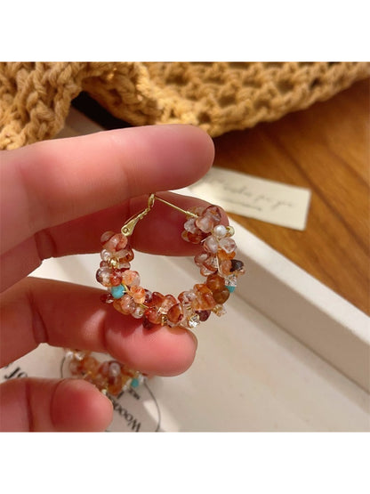 Pair of light tone floral hoop earrings laid flat on a textured surface
