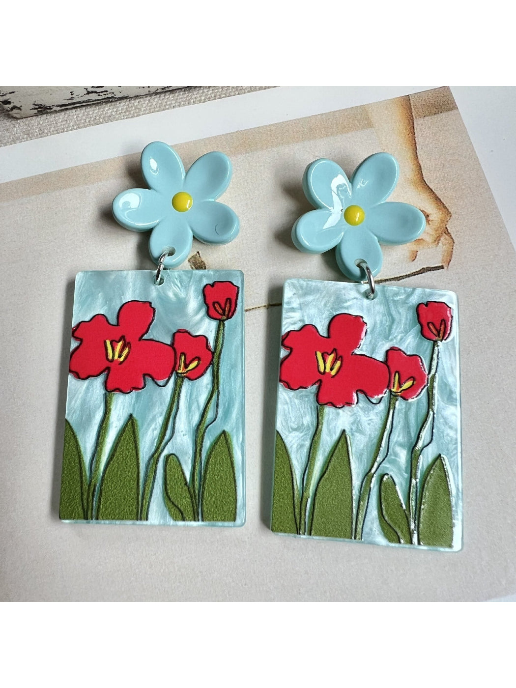 Earwish Painted Flower Drop Earrings hanging on a white display stand