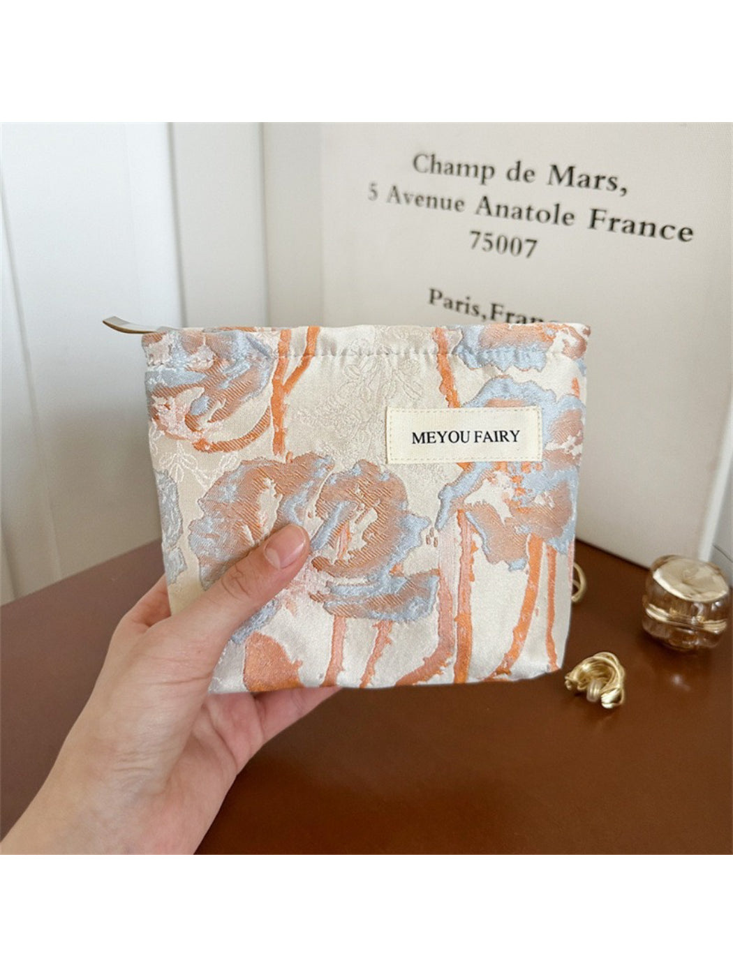 Cosbai cosmetic bag with artistic floral pattern next to makeup items