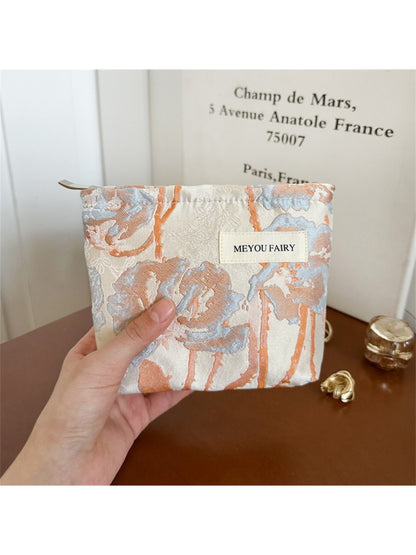 Cosbai cosmetic bag with artistic floral pattern next to makeup items
