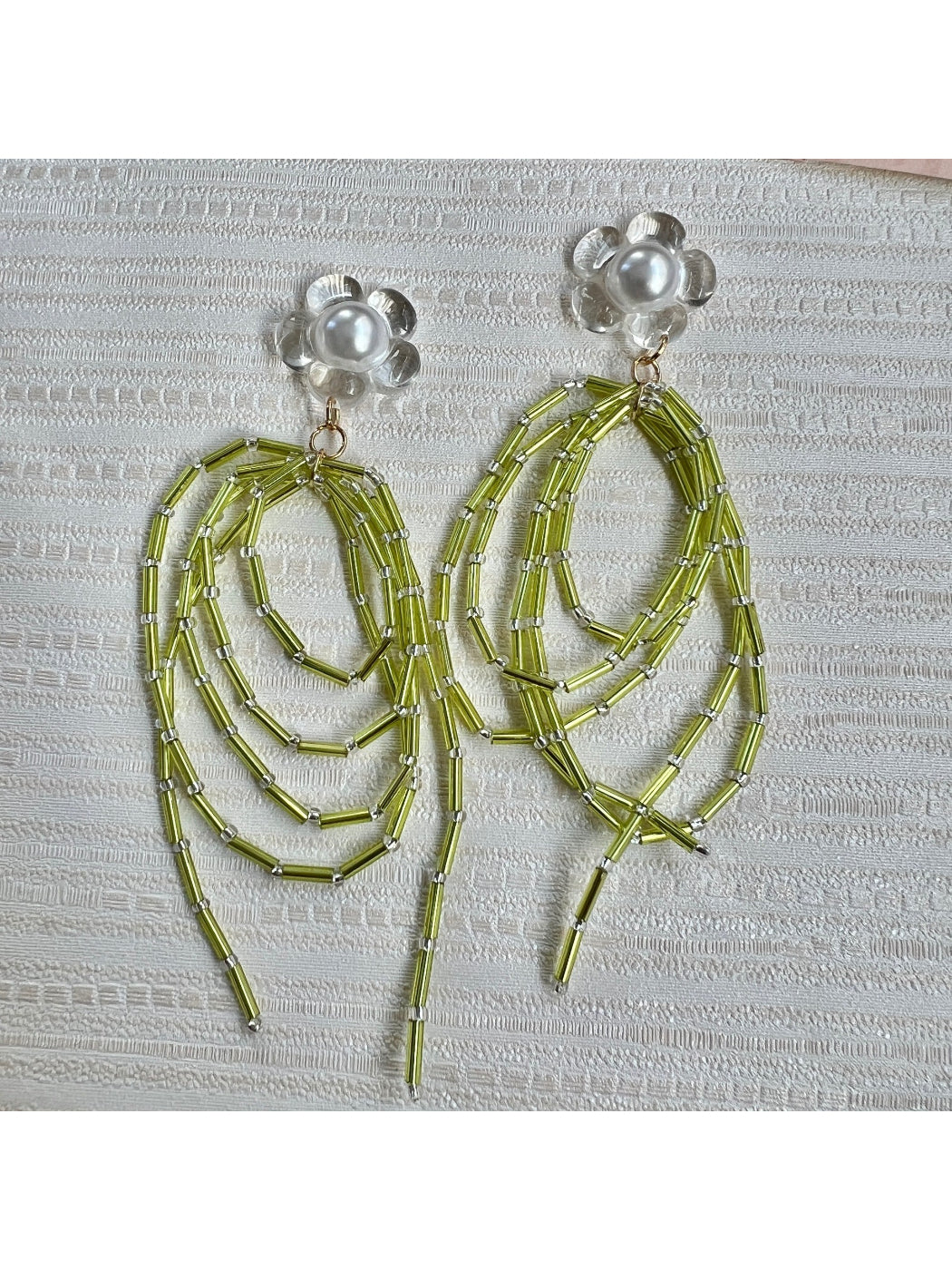 Earwish green bead dangle earrings hanging from a jewelry stand with soft lighting