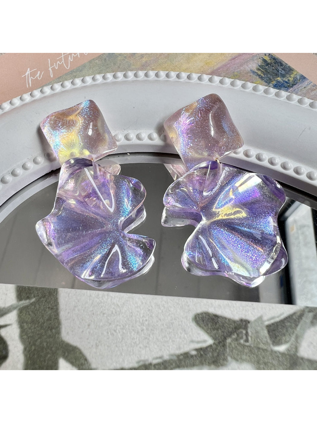 Close-up of Earwish purple flower drop earrings with silver hooks on white background