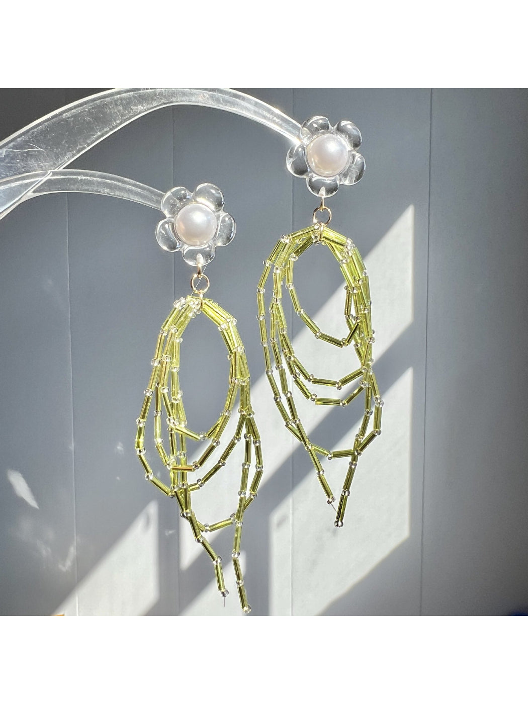 Close-up of Earwish green bead dangle earrings with silver hooks on white background