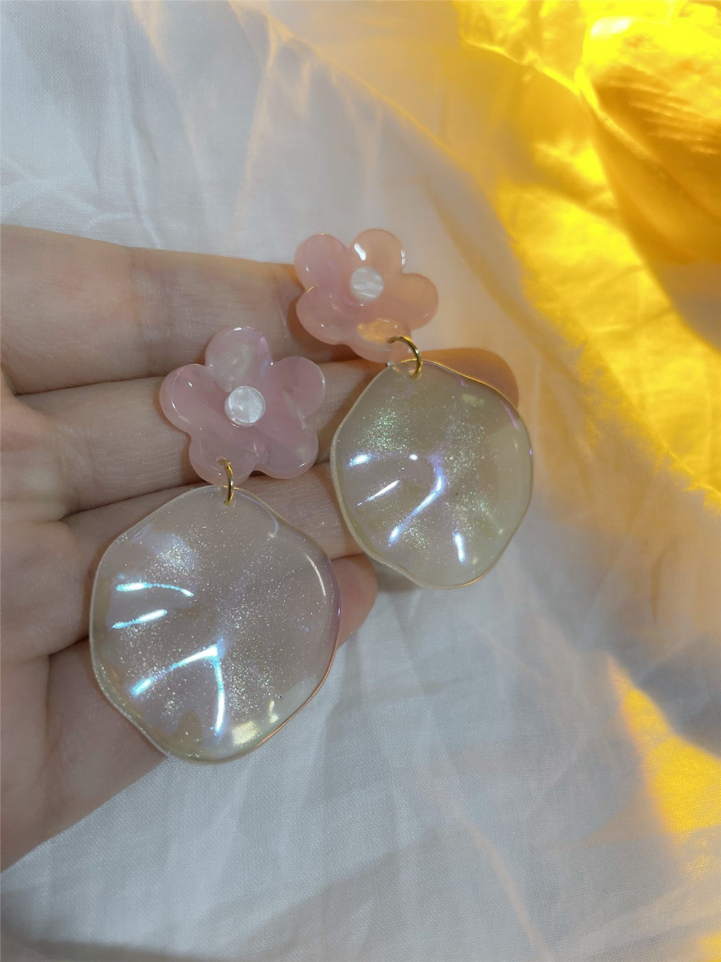 Close-up of glossy floral drop earrings showing detailed petal design