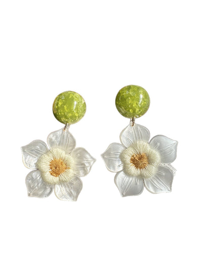 Earwish white flower drop earrings worn on a model's ear with a blurred background