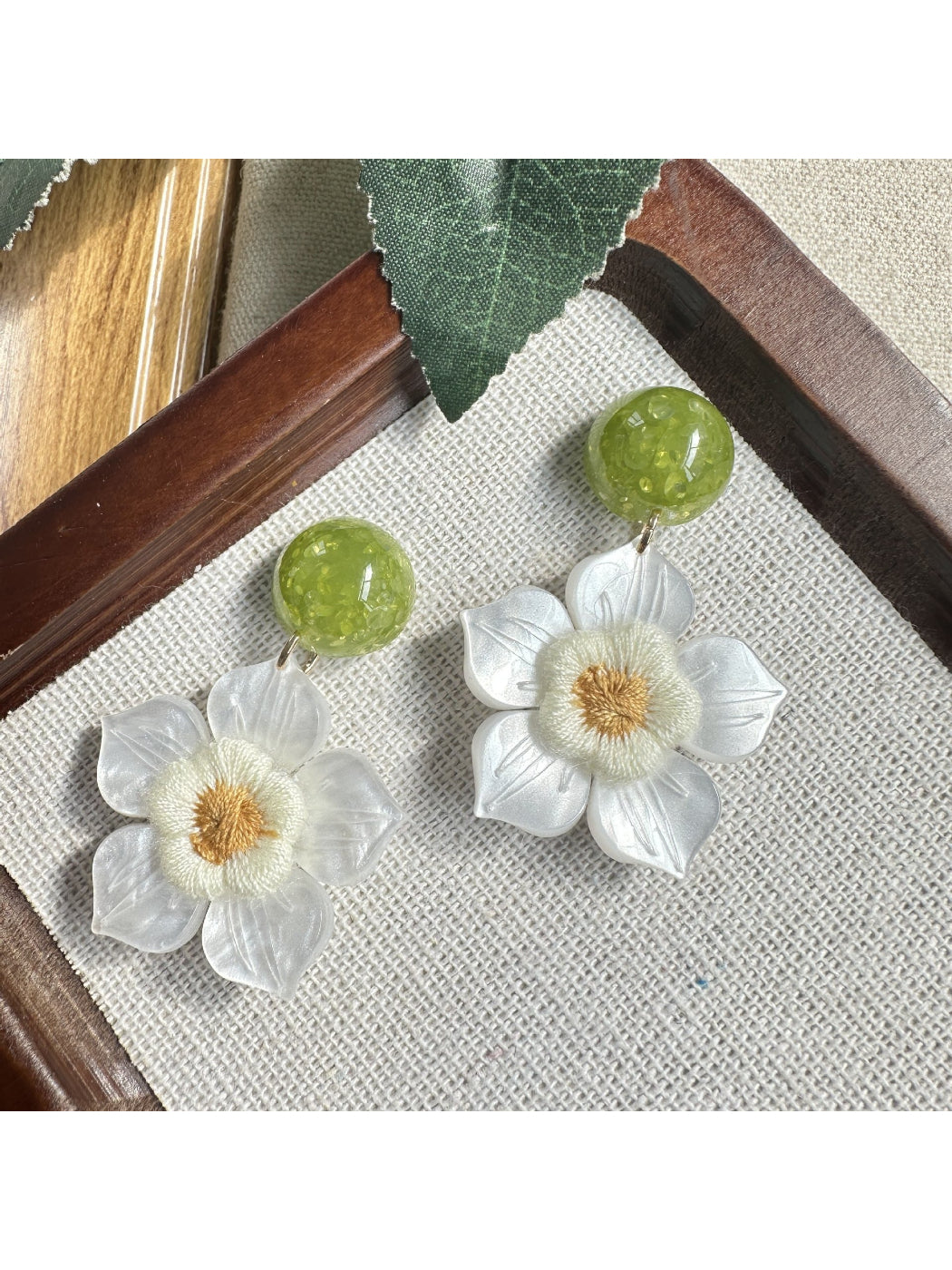Earwish white flower drop earrings displayed on a beige fabric surface