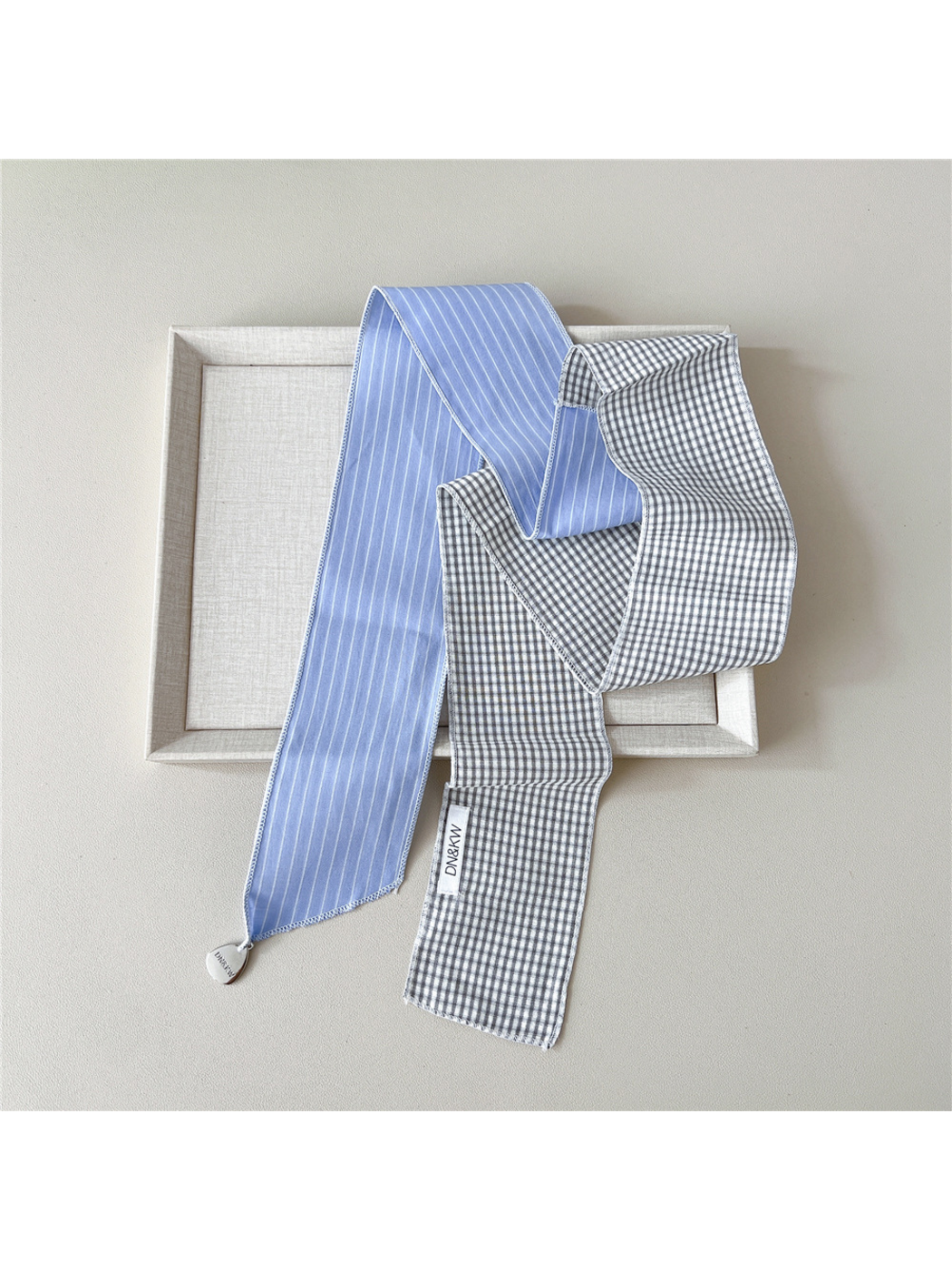 Blue scarf draped untied with white stripes, gray gingham checks and a teardrop charm