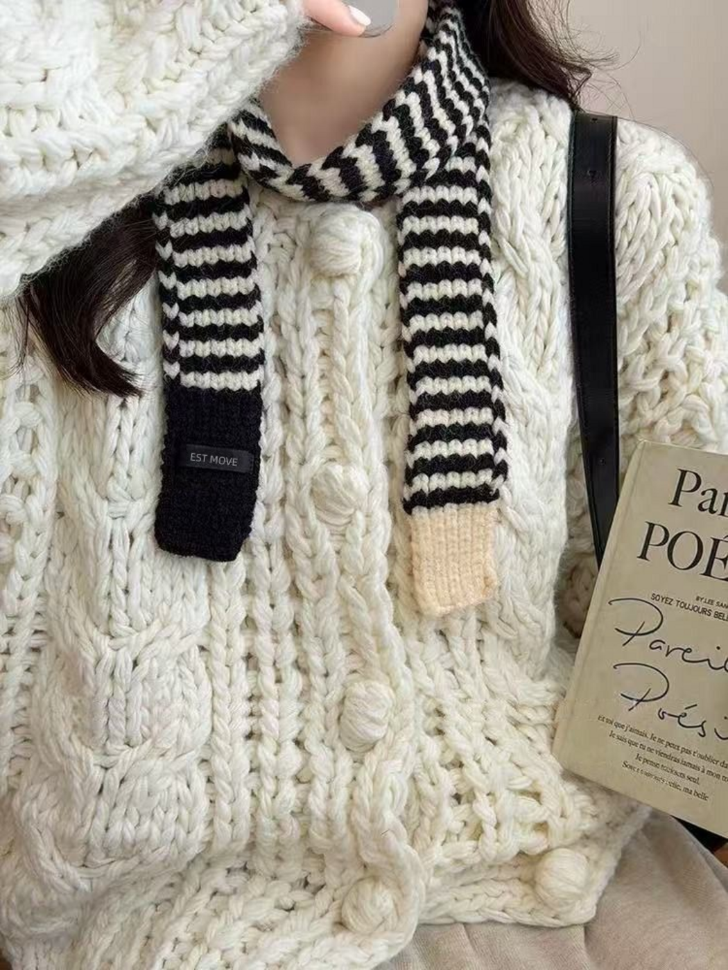 White striped knit scarf draped with both ends hanging over a chunky knit cardigan