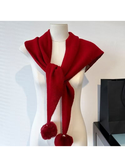 Red knit scarf tied across a mannequin's shoulders, with one pom-pom partly outside the frame