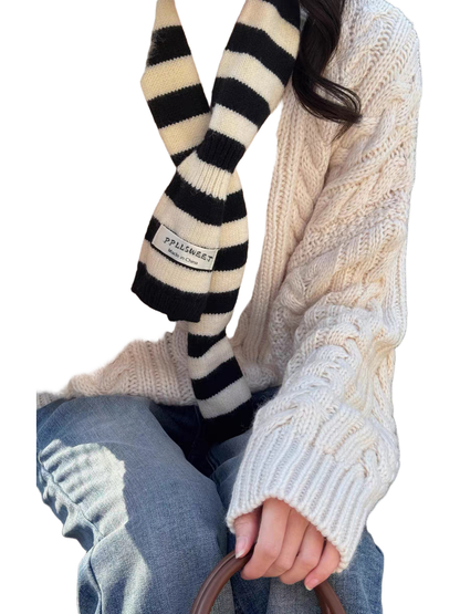 Black striped knit scarf worn outdoors over a cable-knit sweater