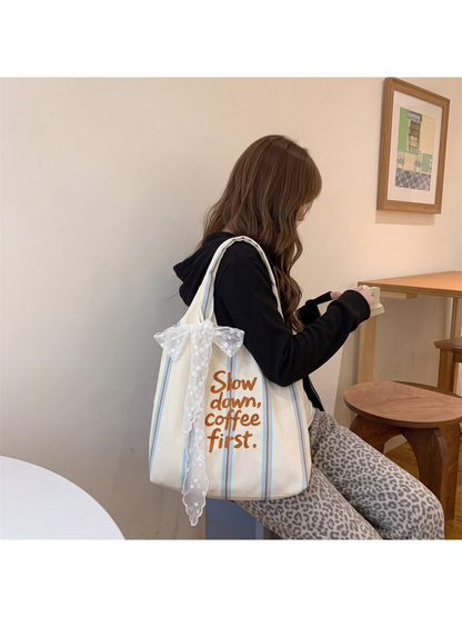 Blue striped tote bag displayed over a shoulder while seated, with a white lace bow