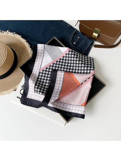 Orange scarf loosely draped across an open box, showing houndstooth panels, striped sections and hemmed edges