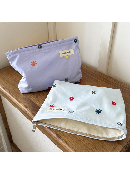 Purple makeup bag standing behind an open Blue floral bag showing its cream-colored interior