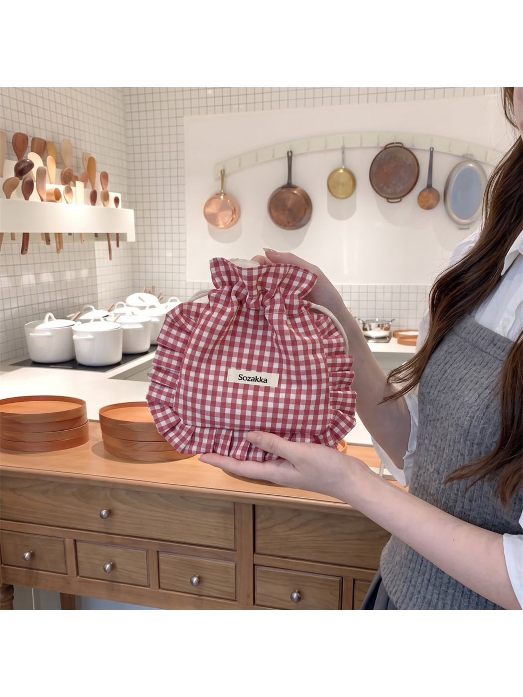 Burgundy gingham drawstring pouch held upright with its ruffled trim spread