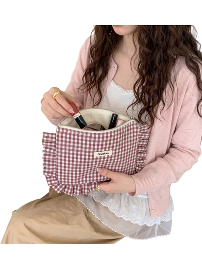 Burgundy gingham cosmetic pouch held open with cosmetics visible inside