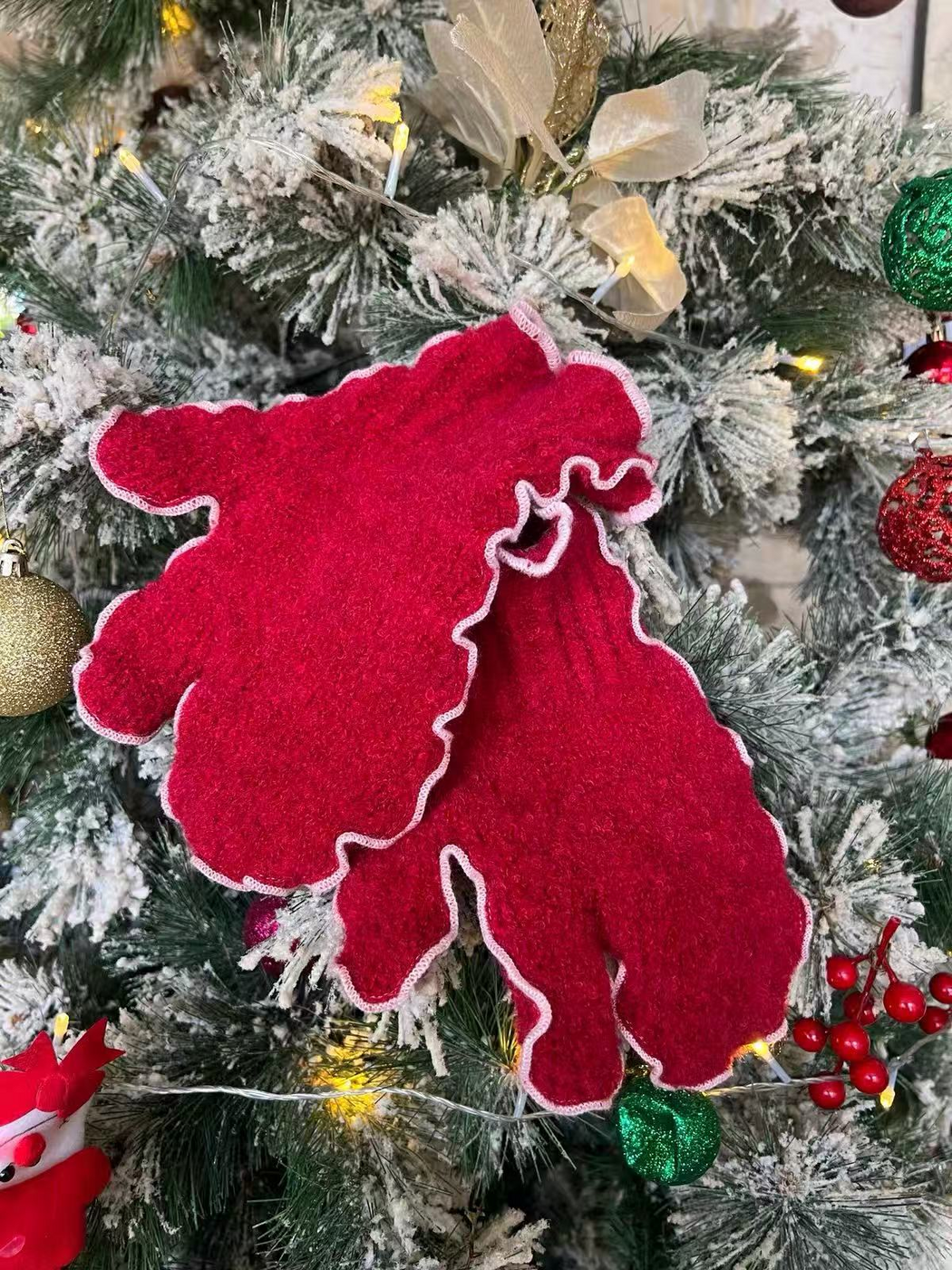 Red mittens with pale ruffled edging displayed on a decorated tree