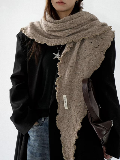Knit scarf wrapped across the shoulders with a long scalloped end over a black jacket