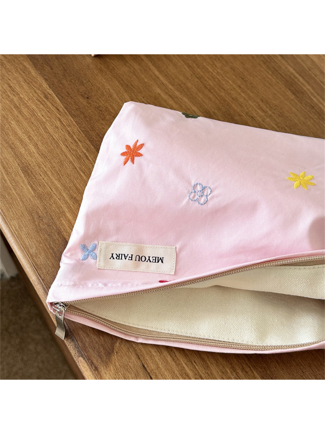 Close-up of Pink floral makeup bag embroidery, sewn label and cream-colored interior