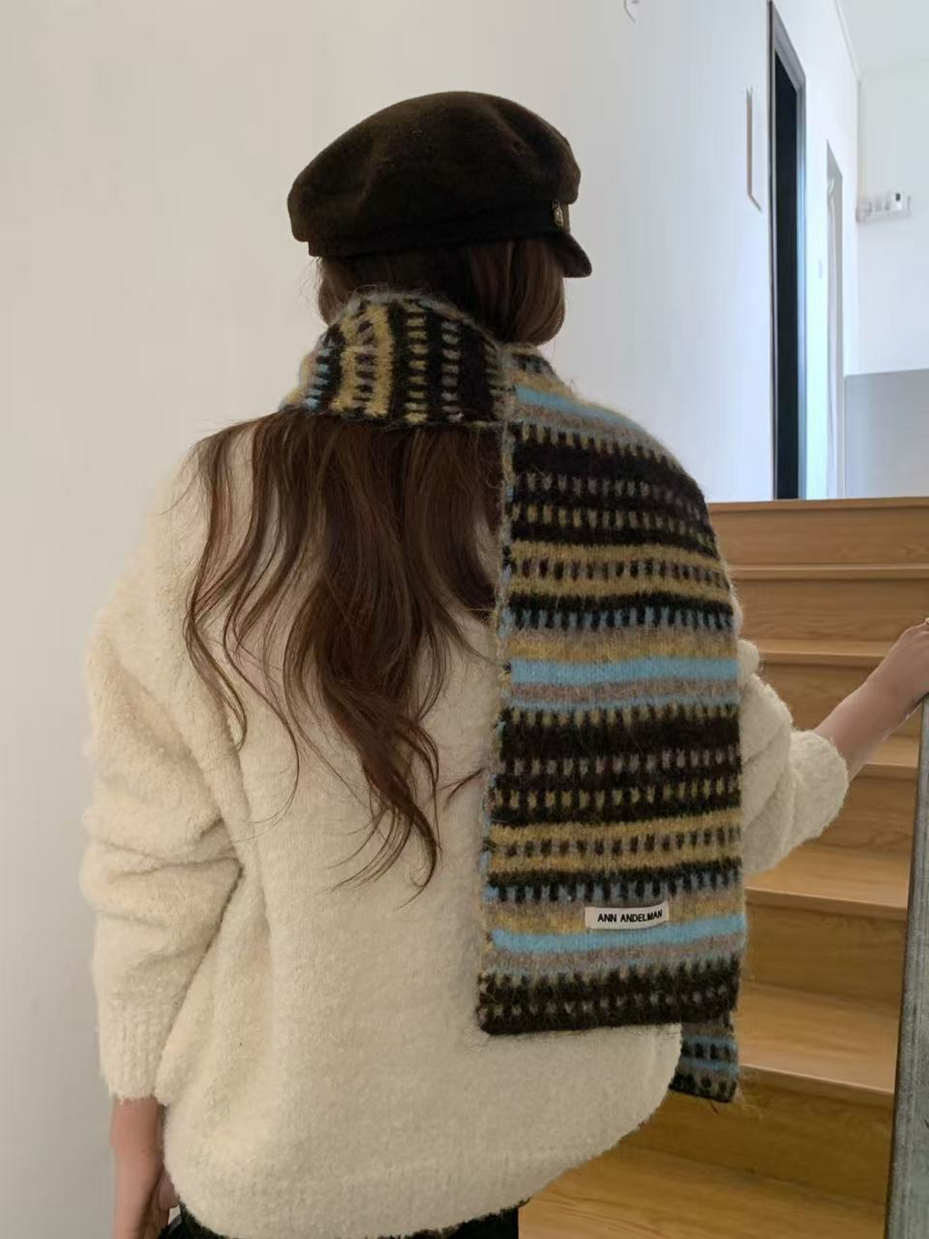 Brown striped scarf worn around the neck with one end hanging down the back