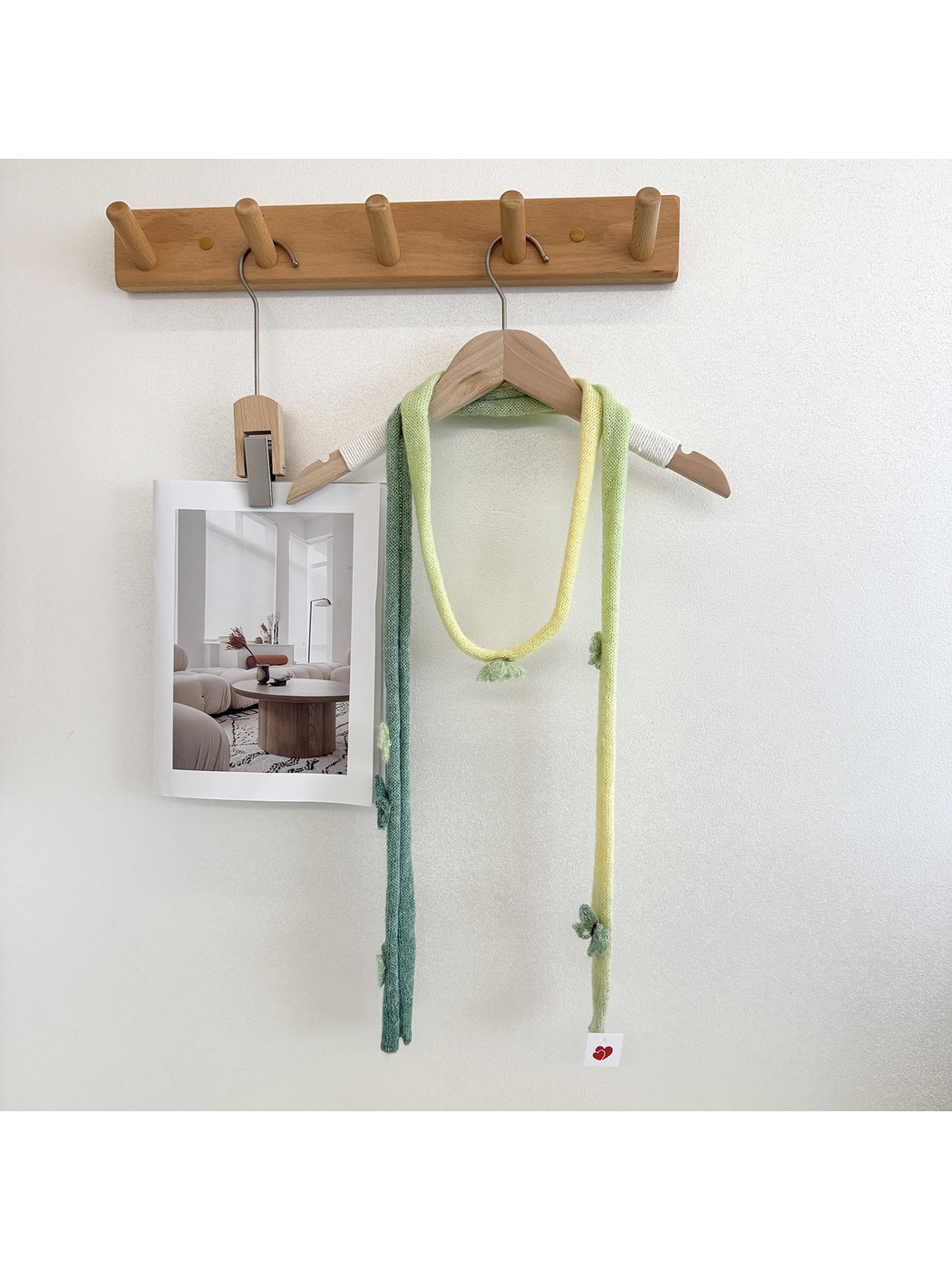 Green knit scarf with yellow gradient sections and raised embellishments looped over a wooden hanger