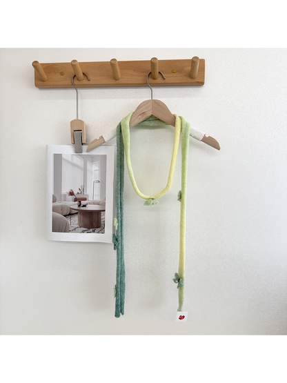 Green knit scarf with yellow gradient sections and raised embellishments looped over a wooden hanger