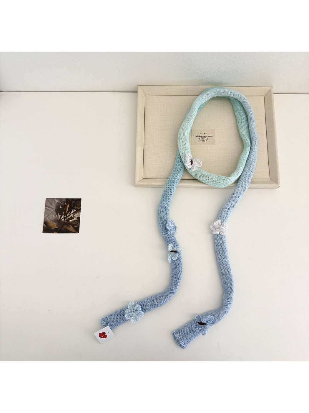 Blue knit scarf laid in a long loop showing mint sections and raised flower and butterfly embellishments