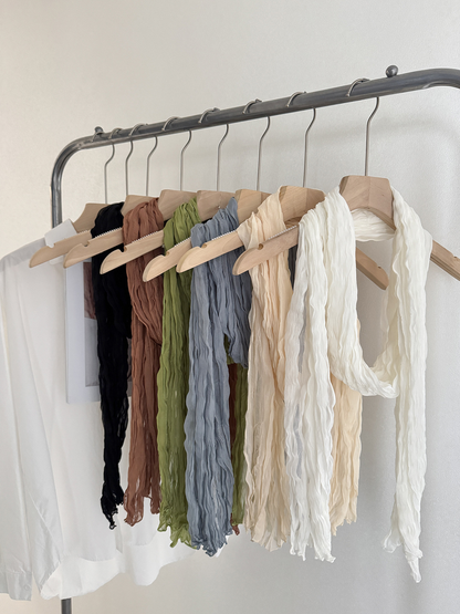 Several crinkled scarves hanging together with a White scarf in front