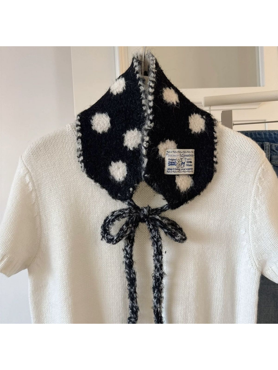 Black polka-dot hood-shaped scarf tied in a bow over a white sweater