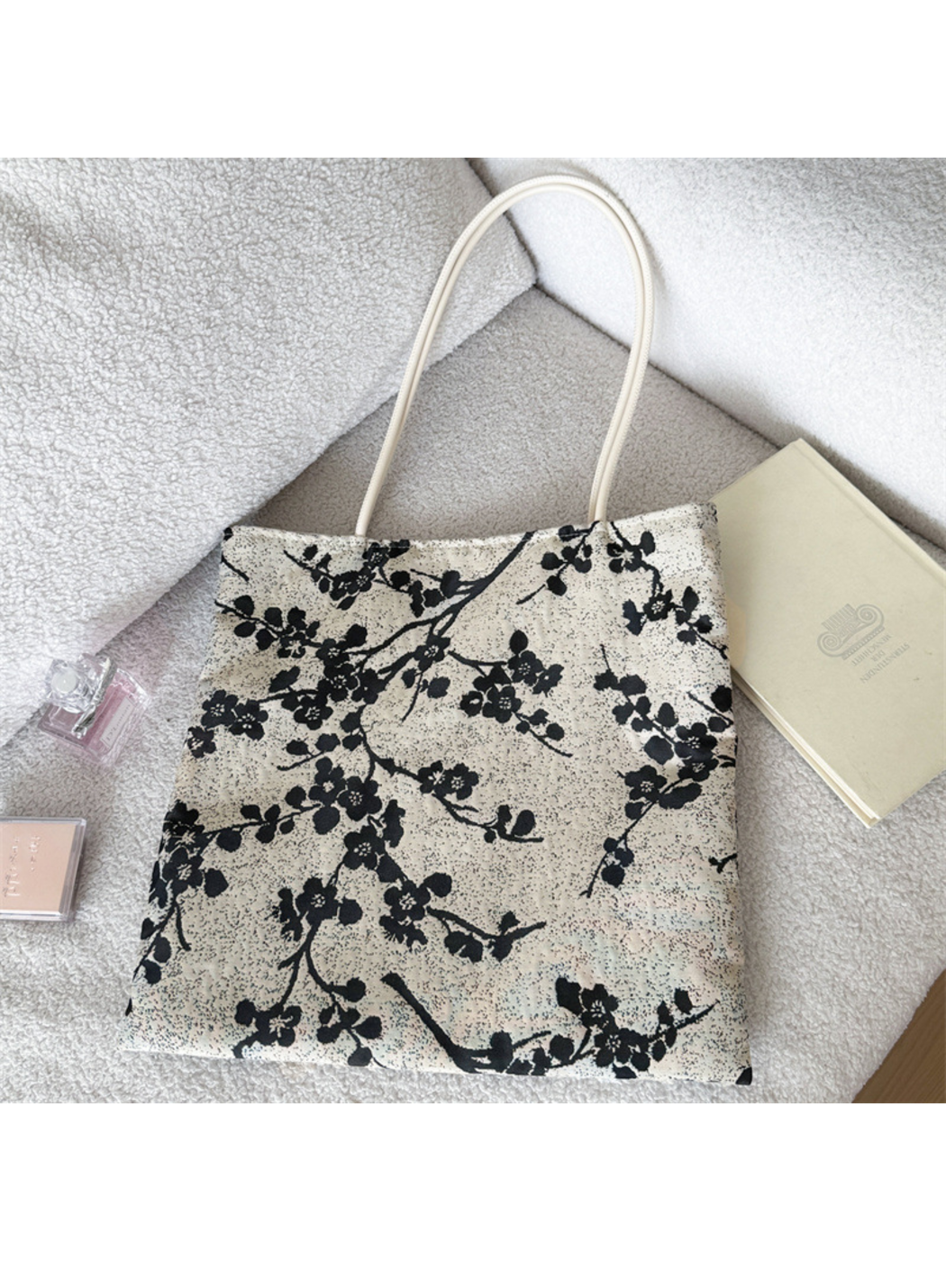 Black tote bag showing the reverse flowering-branch arrangement on a light speckled ground