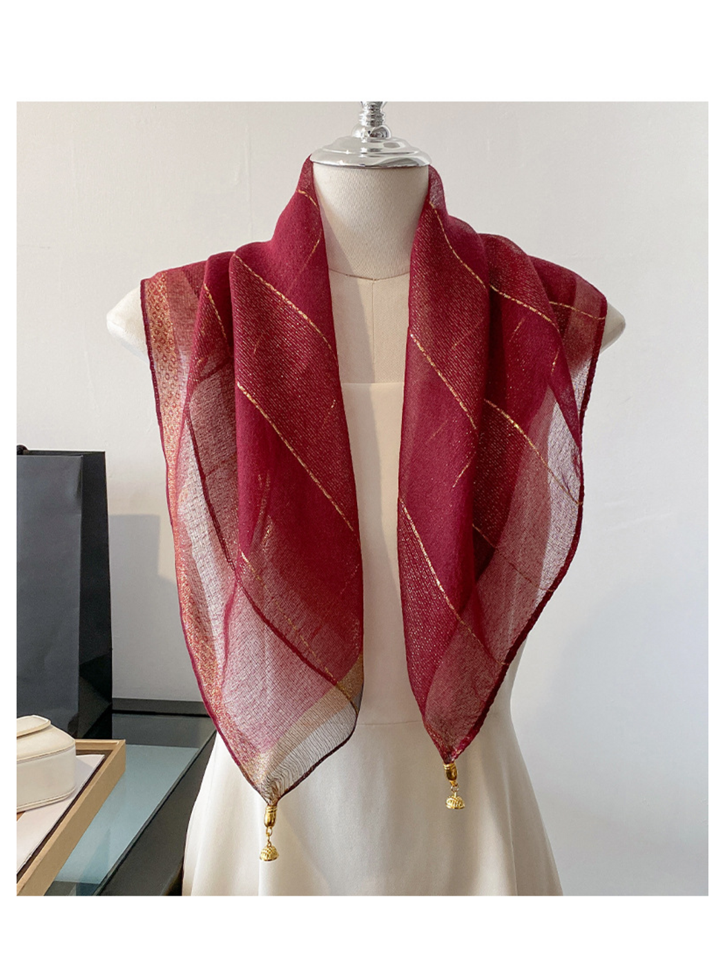 Burgundy scarf draped on a mannequin with metallic-look lines and gold-tone end ornaments