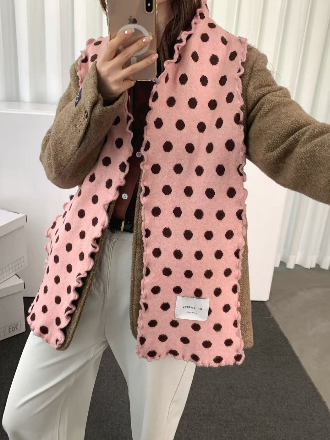 Pink polka dot scarf draped with both ends hanging over a brown jacket