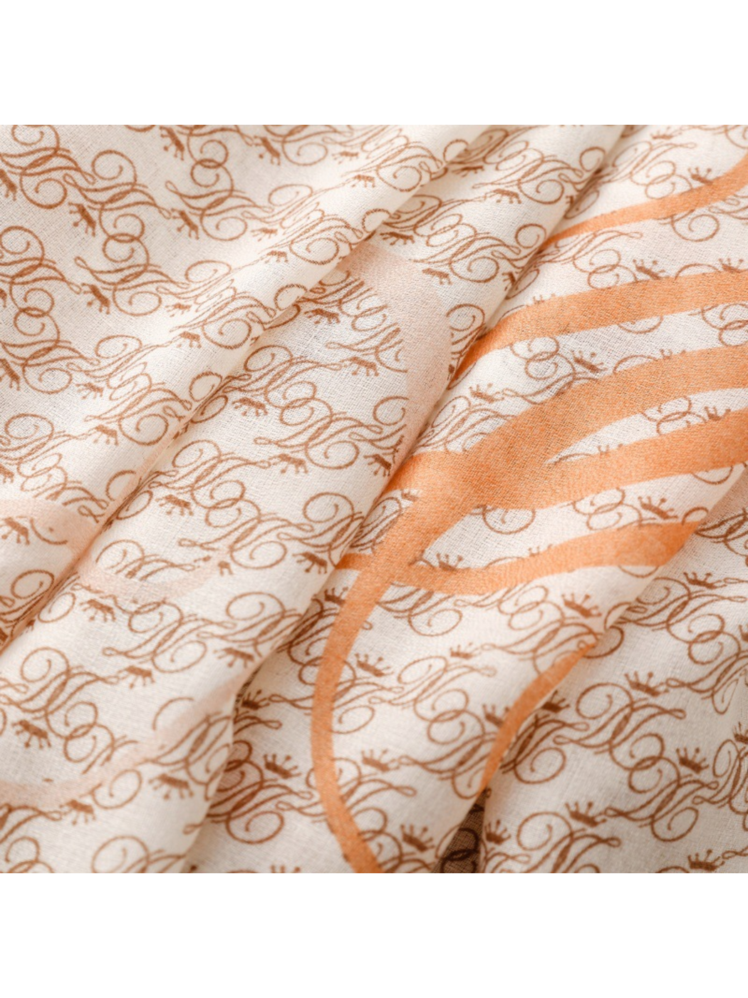 Close-up of brown ornate motifs and a broad orange scroll across ivory scarf folds