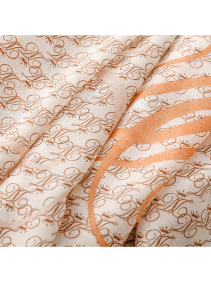 Close-up of brown ornate motifs and a broad orange scroll across ivory scarf folds