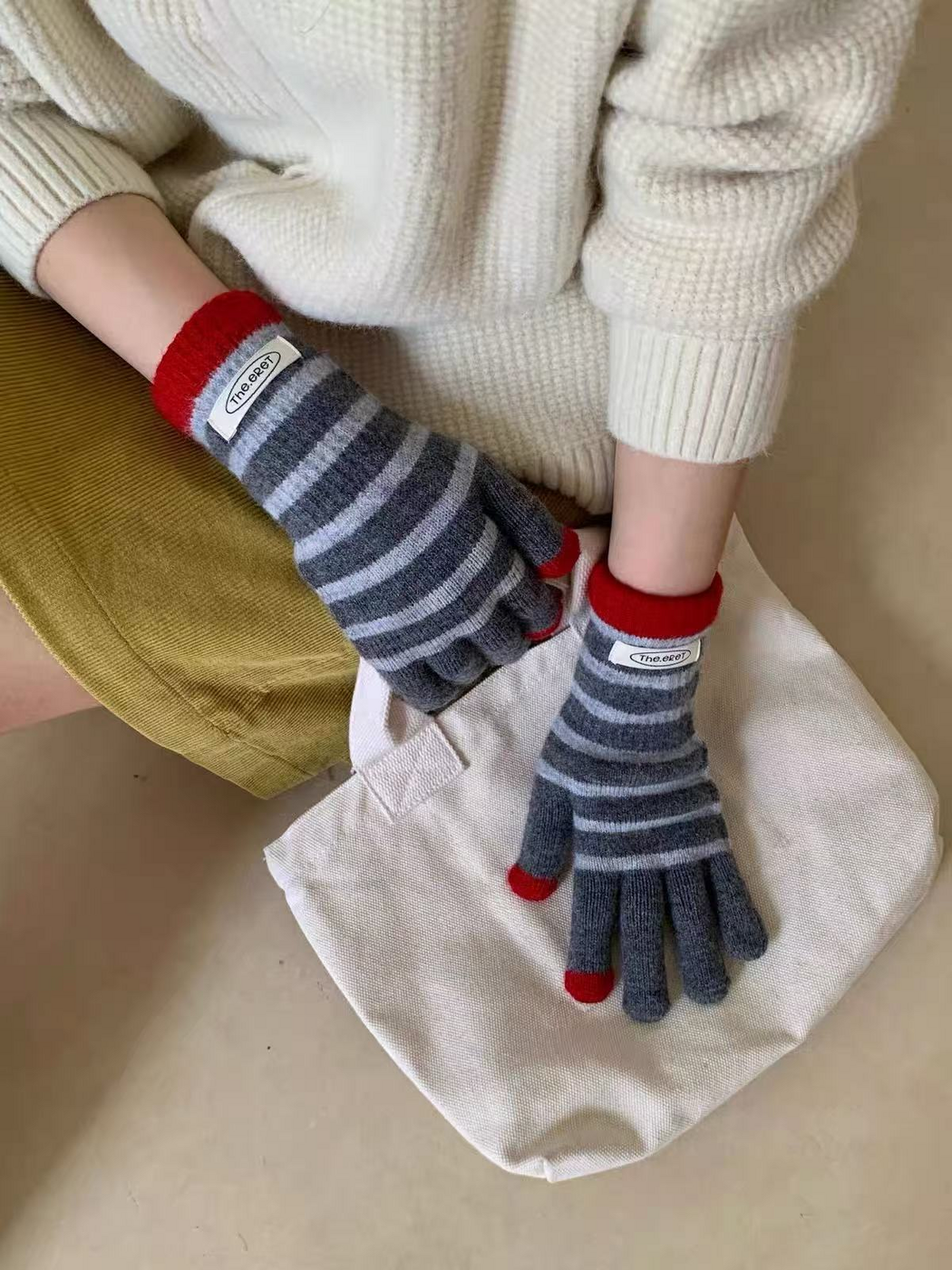 Gray striped gloves worn while holding a cream tote bag