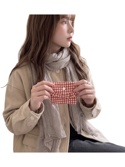 Red gingham coin purse held at chest level, showing the curved ruffled flap